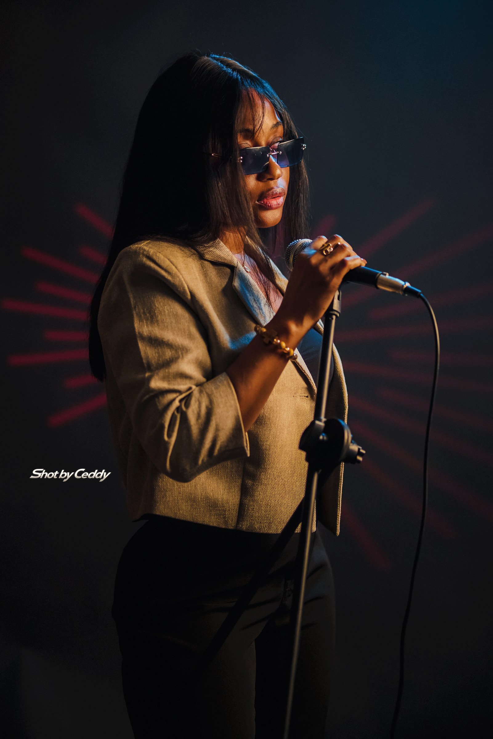 Studio portrait in sunglasses and a gold jacket beside a microphone stand.