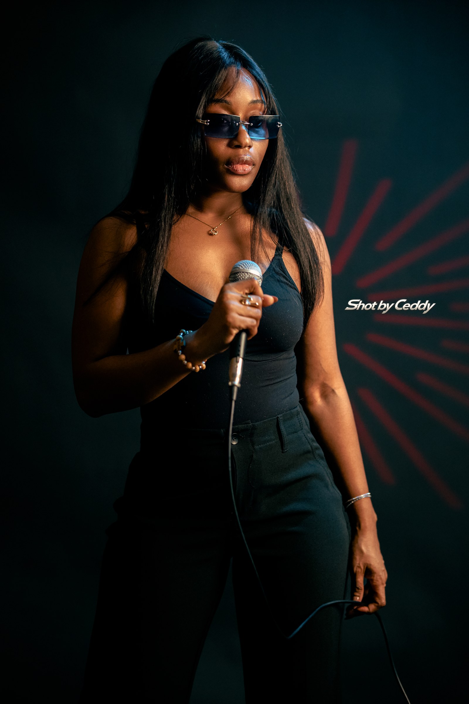 Portrait in a black outfit holding a microphone against a red and teal studio backdrop.