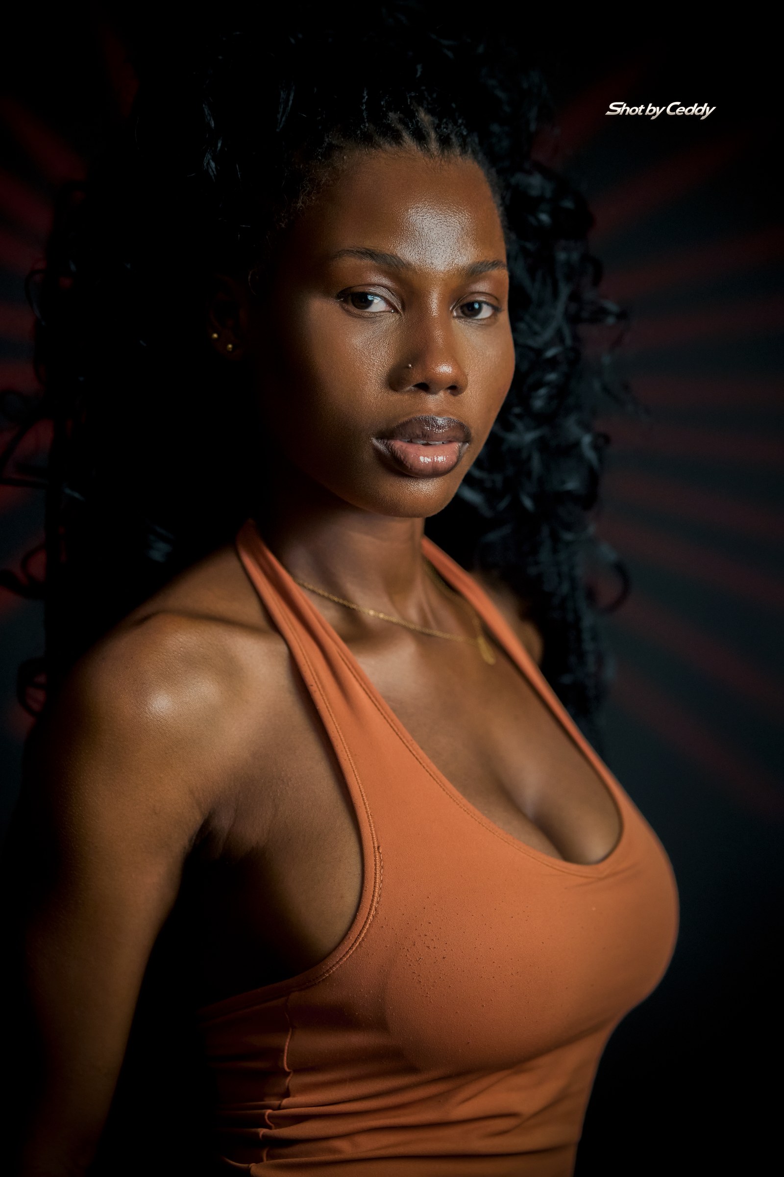 Close three-quarter portrait in an orange halter top against a dark background.