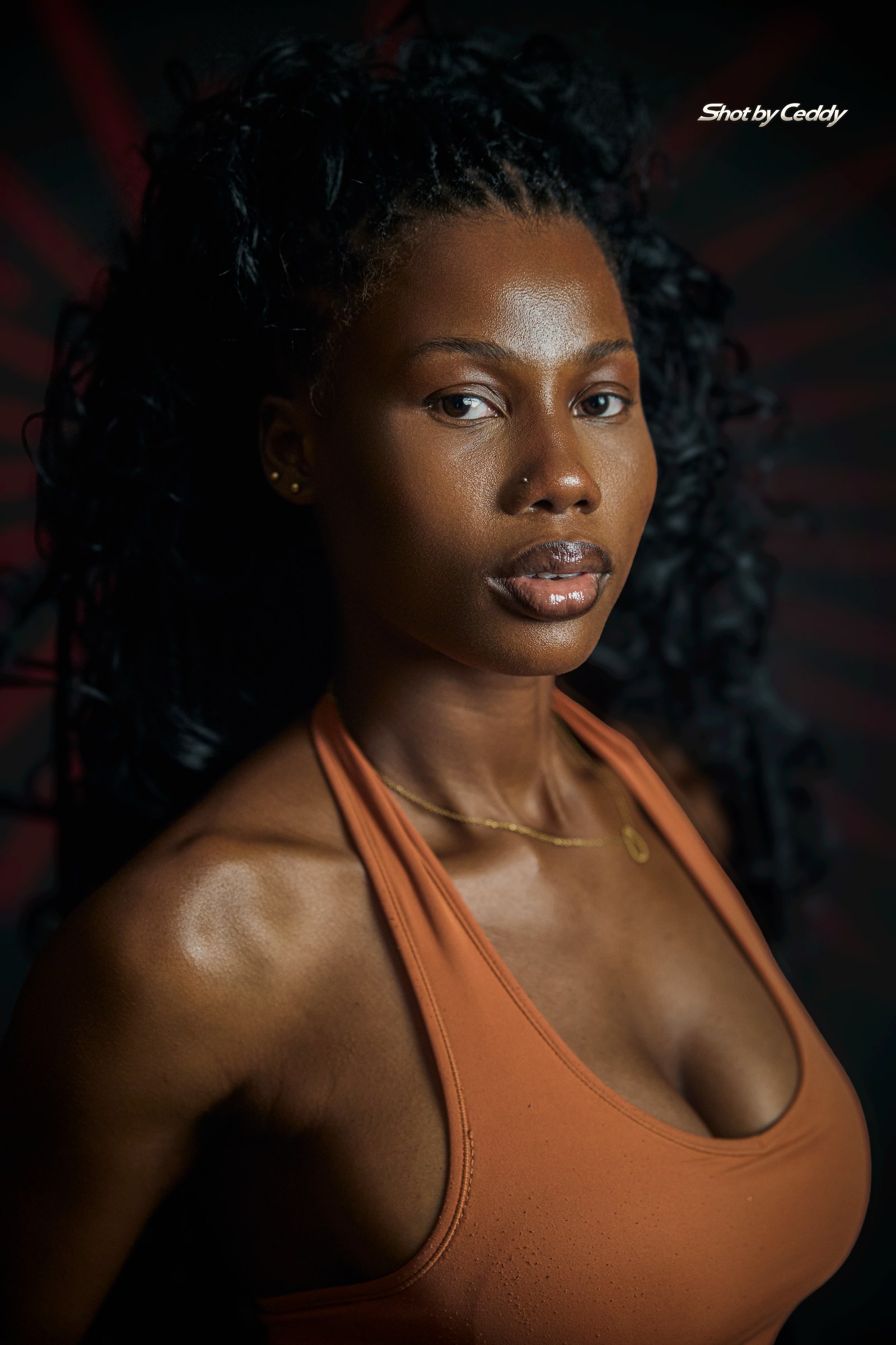 Close portrait with a softly lit face and an orange halter top.